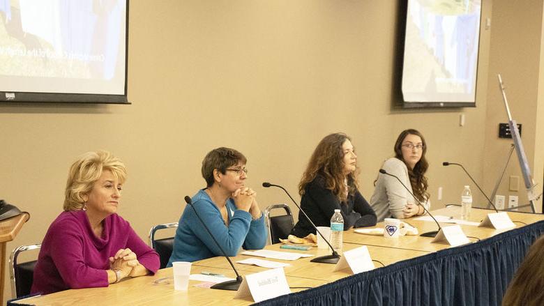 four women sit at table with microphones at panels